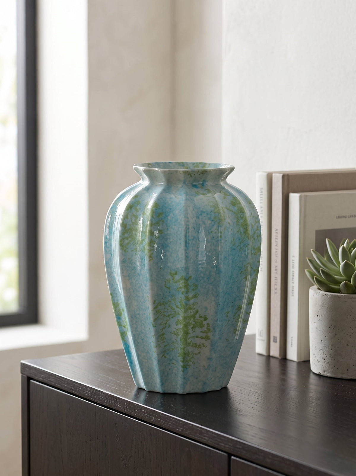 Ocean blue spotted fluted ceramic vase, empty, on a dark sideboard beside a window