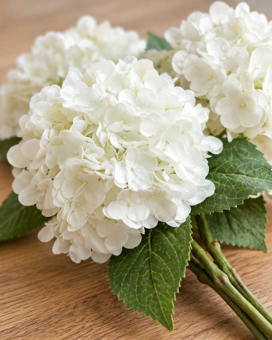 Close-up detail of the white artificial hydrangea stems on an oak table