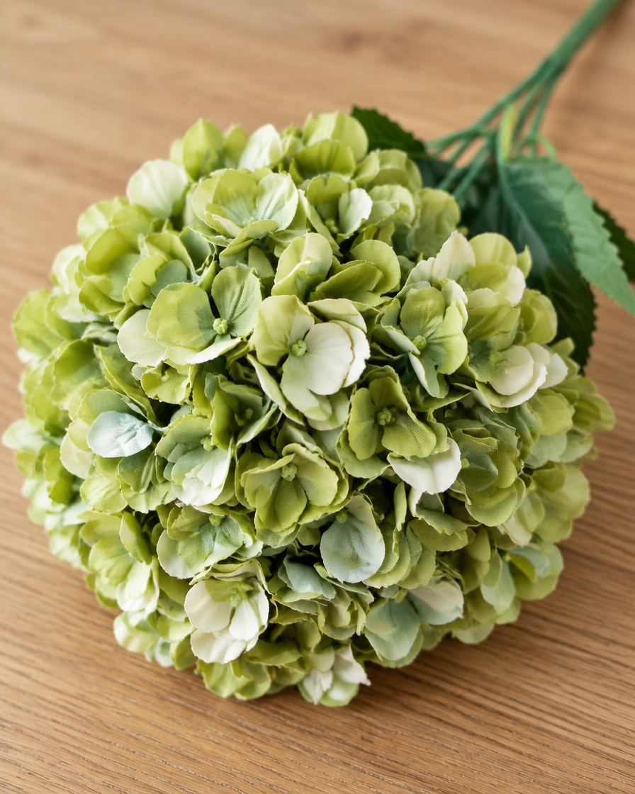 Close-up detail of the sage green artificial hydrangea stem on an oak table