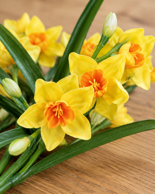 Close-up detail of the yellow artificial narcissus stems on an oak table