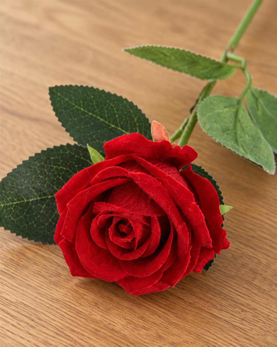 Close-up detail of the red artificial rose on an oak table