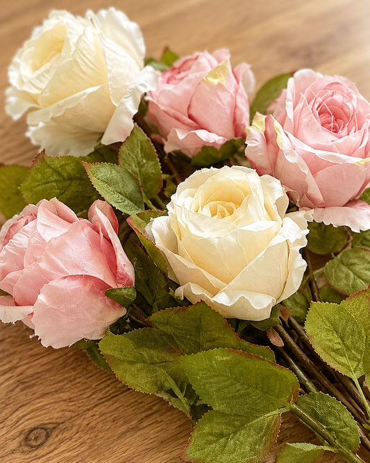 Close-up detail of the pink and cream artificial rose stems on an oak table