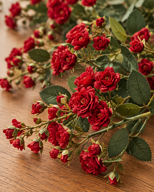 Close-up detail of the red artificial spray rose stems on an oak table