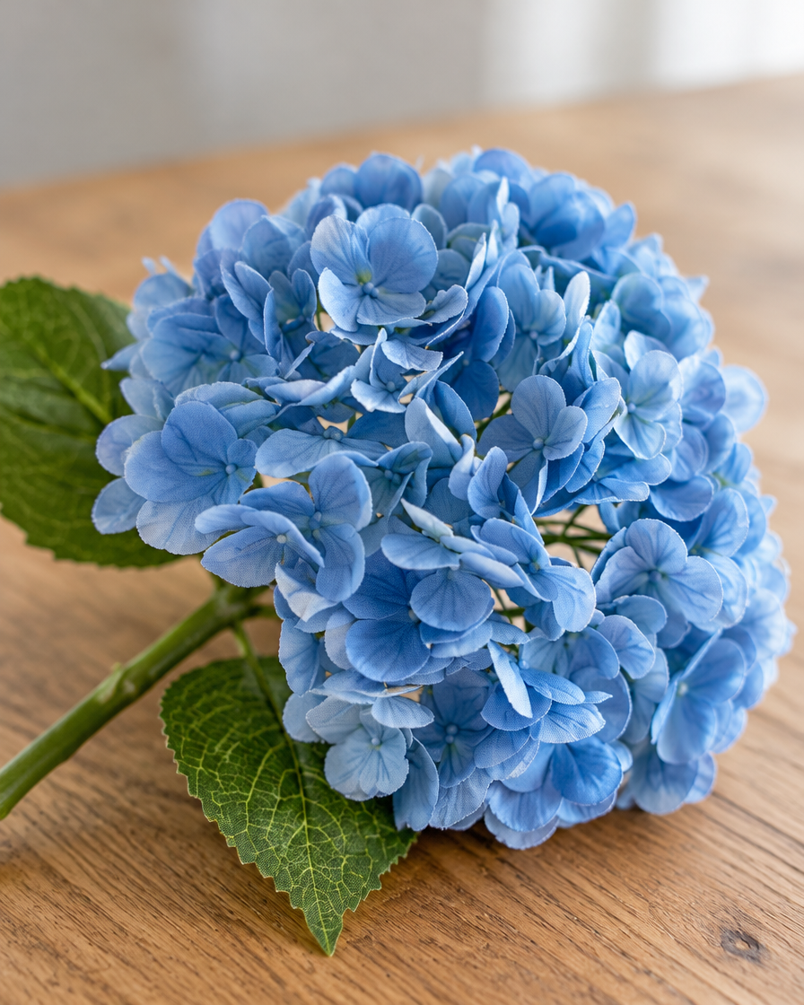 Close-up detail of the blue artificial hydrangea stem on an oak table