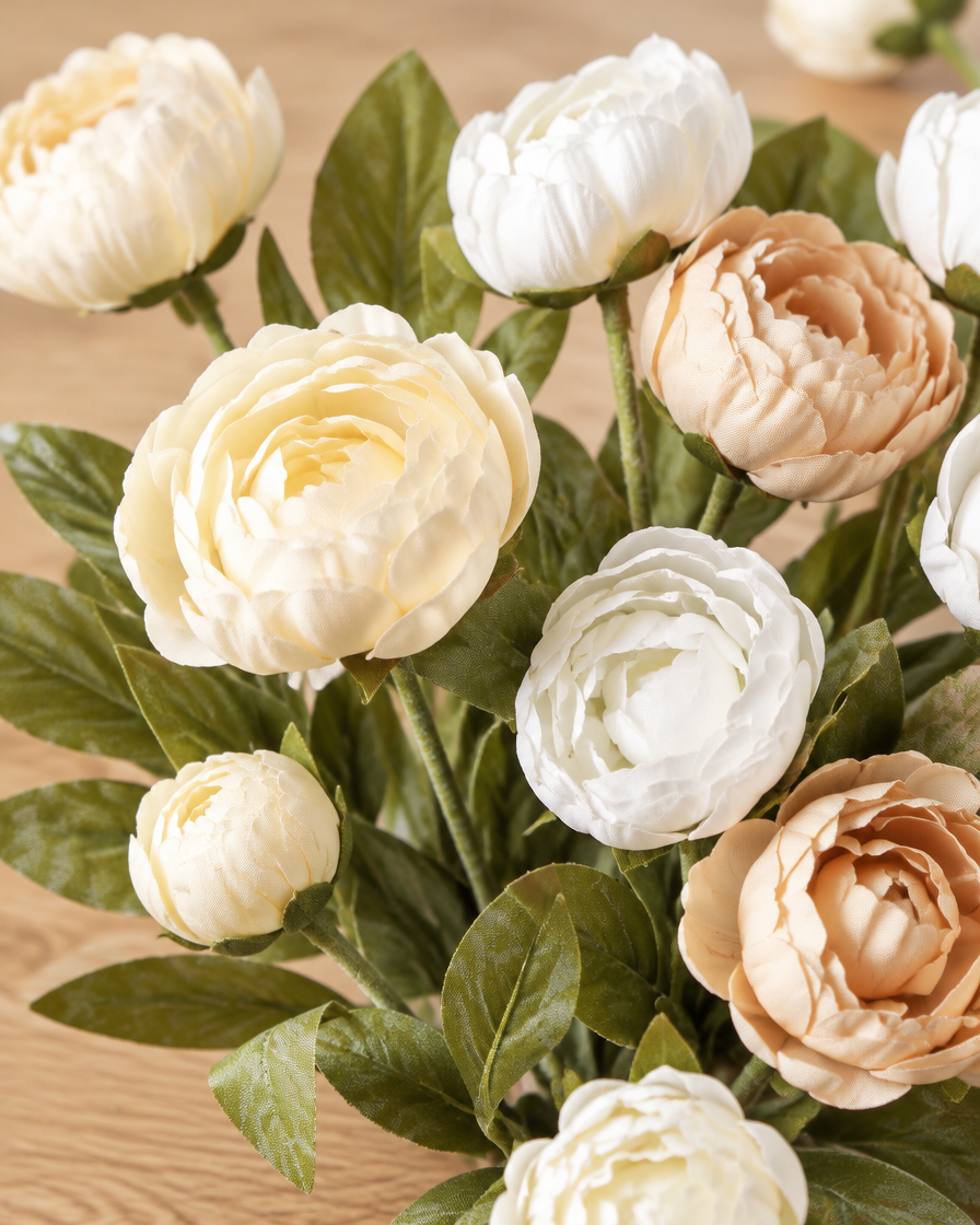Close-up detail of the cream and apricot artificial ranunculus stems on an oak table