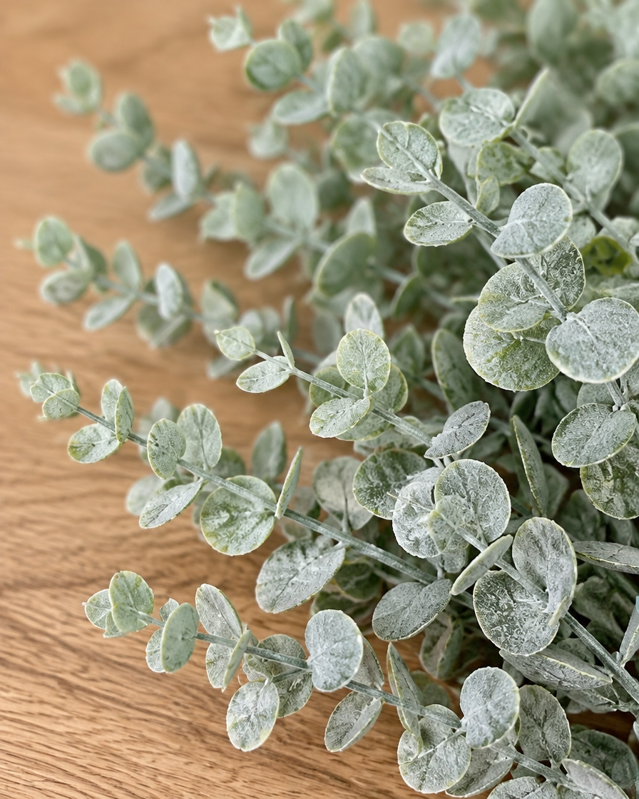 Close-up detail of the frosted sage artificial eucalyptus stems on an oak table