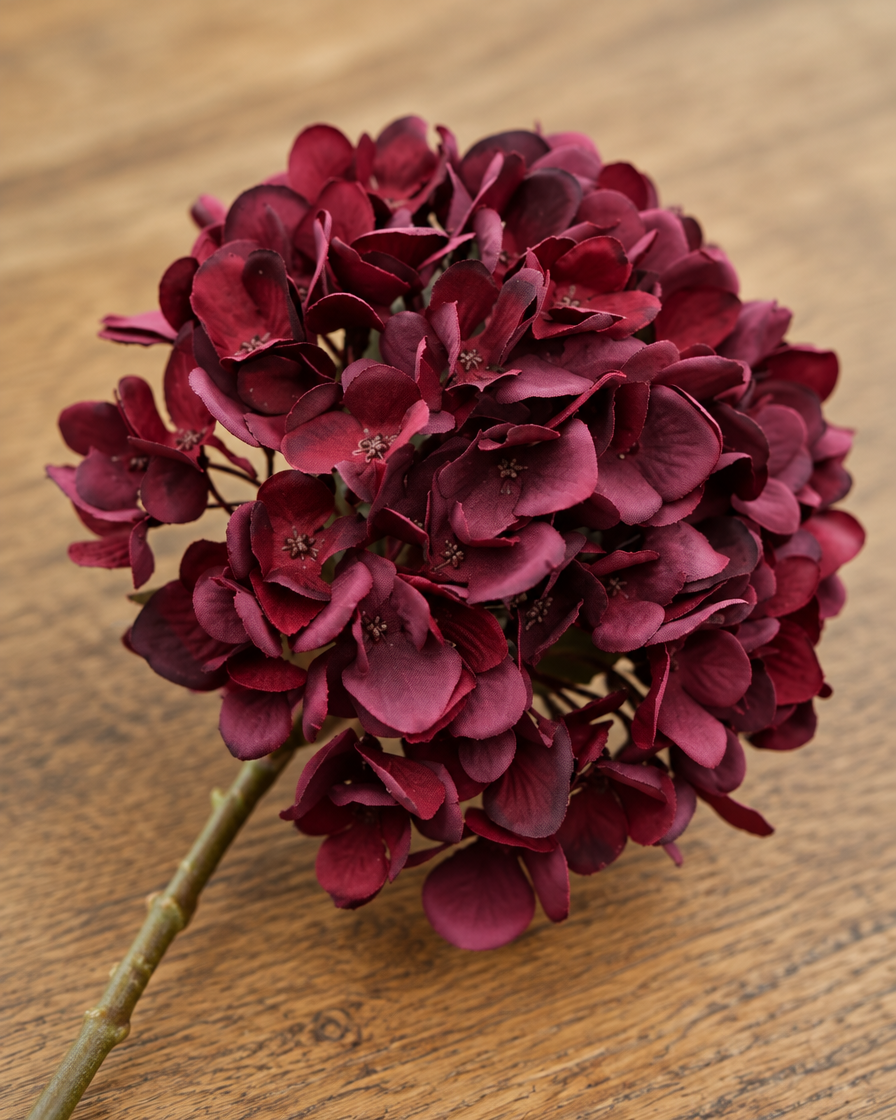 Close-up detail of the burgundy artificial hydrangea stem on an oak table