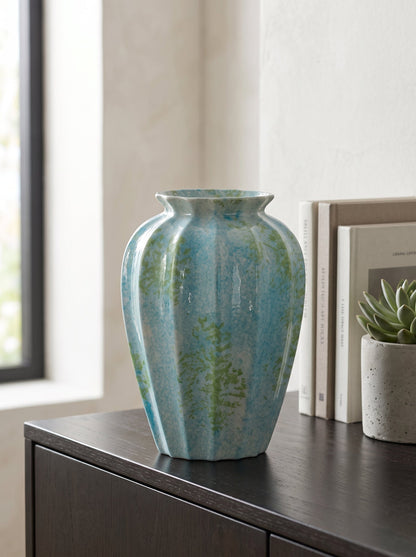 Ocean blue spotted fluted ceramic vase, empty, on a dark sideboard beside a window