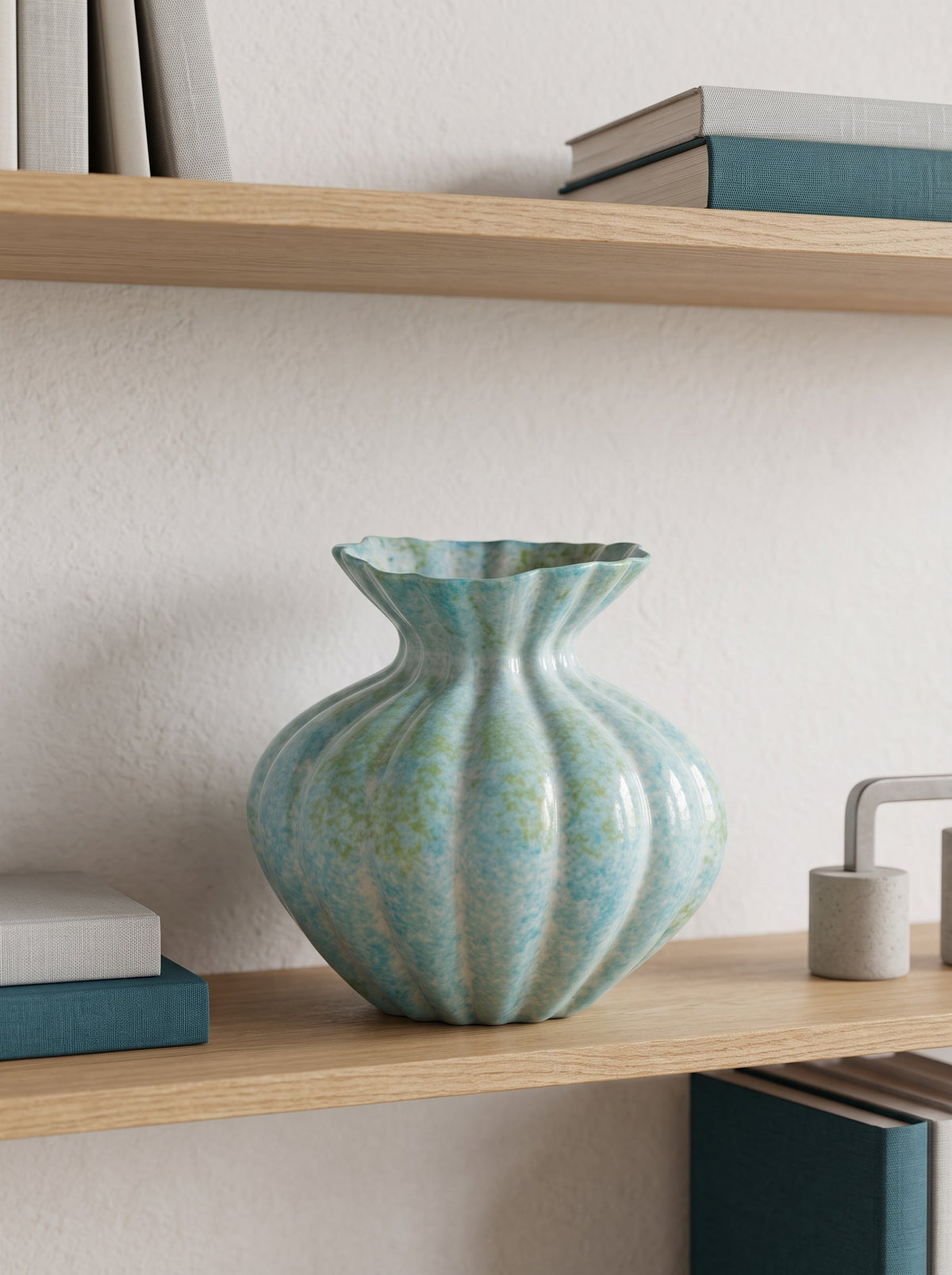 Mint blue fluted ceramic vase, empty, on a wooden shelf with books