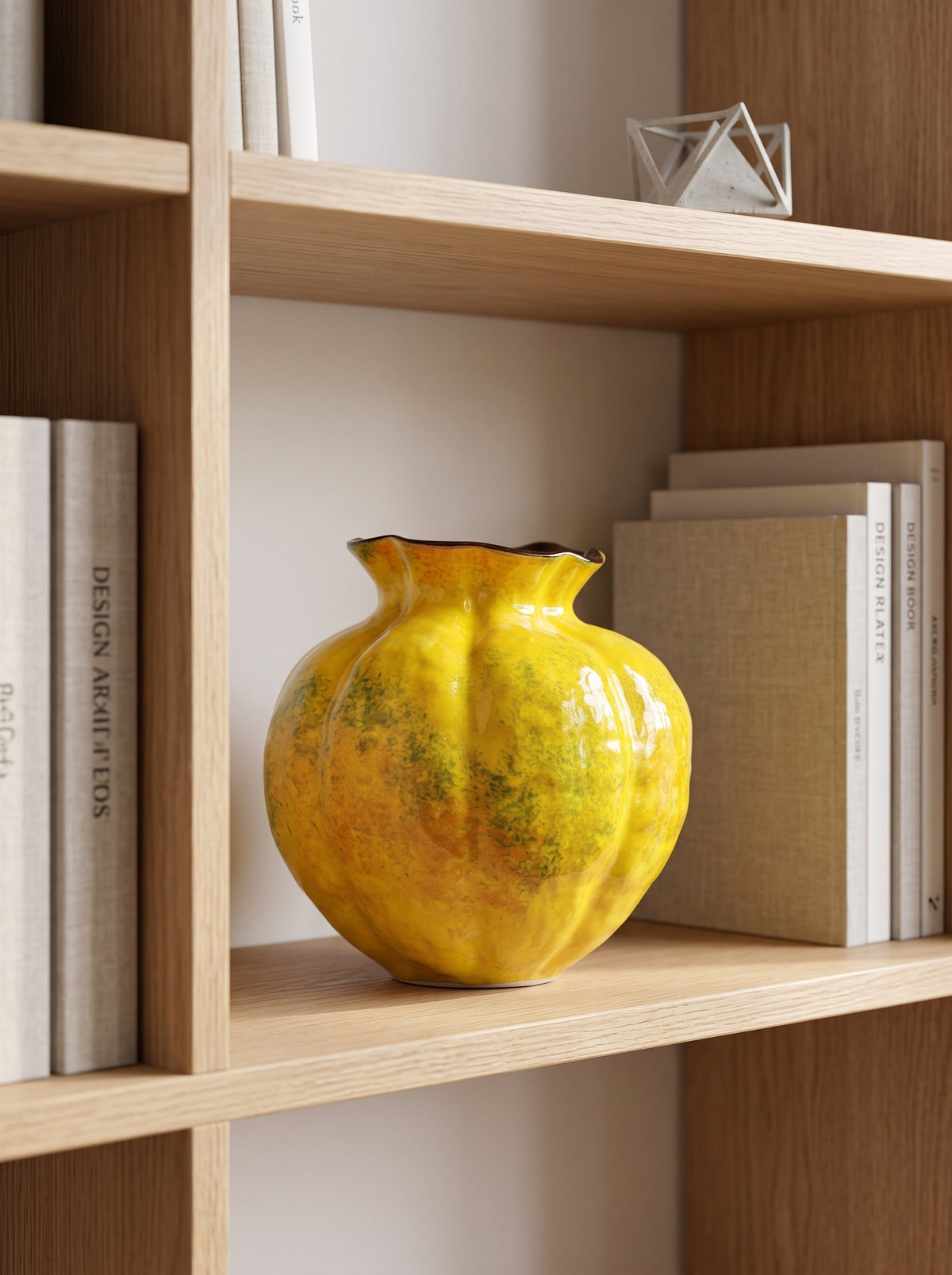 Yellow speckled fluted glazed vase, empty, on a wooden shelf among books