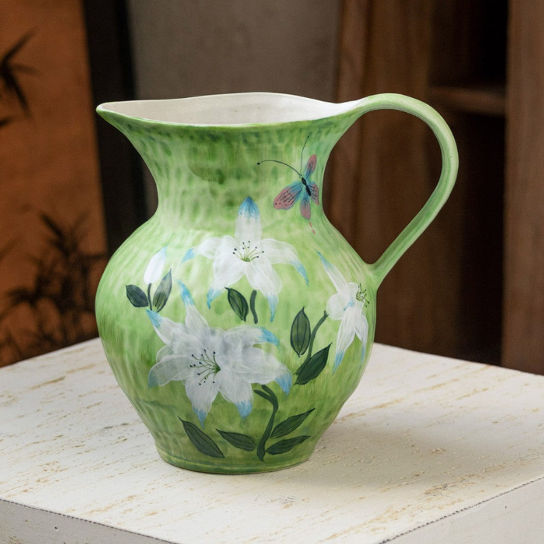 Green ceramic pitcher-style vase with a white lily design and a side handle on a white surface
