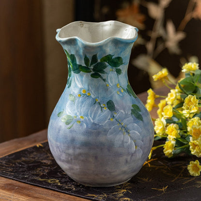 Blue-grey ceramic vase with dark green wisteria painting and a wavy rim beside yellow flowers
