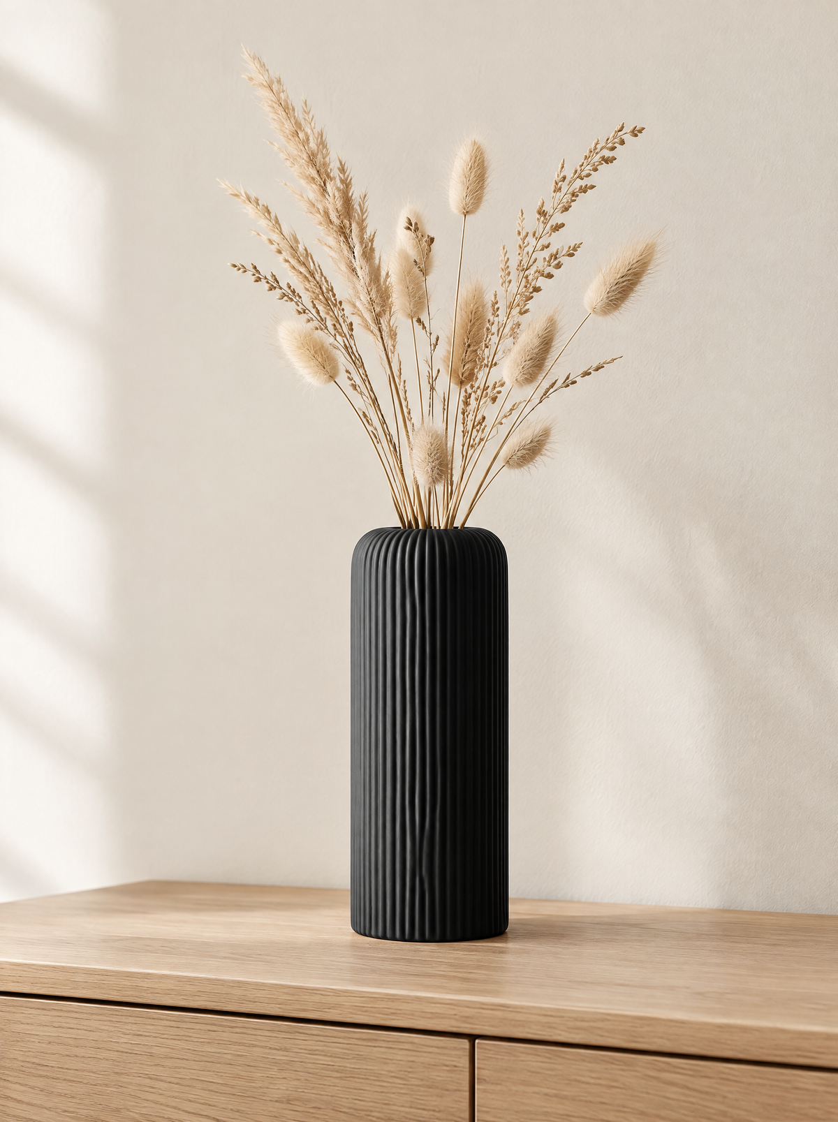 Tall matte black ceramic vase with fine vertical grooves on a light oak console with dried grass stems