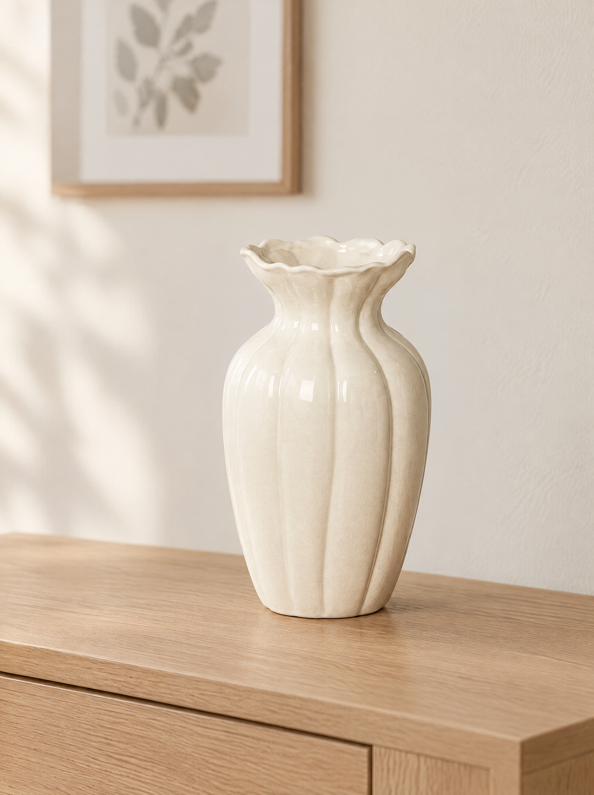Cream fluted glazed ceramic vase with ruffled rim on a light oak console