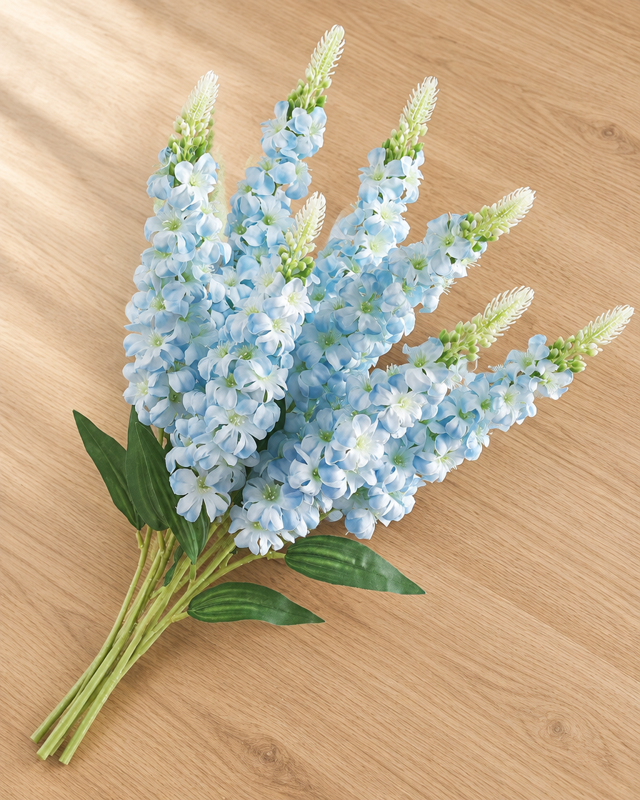 Close-up detail of the light blue artificial delphinium flower stems on an oak table