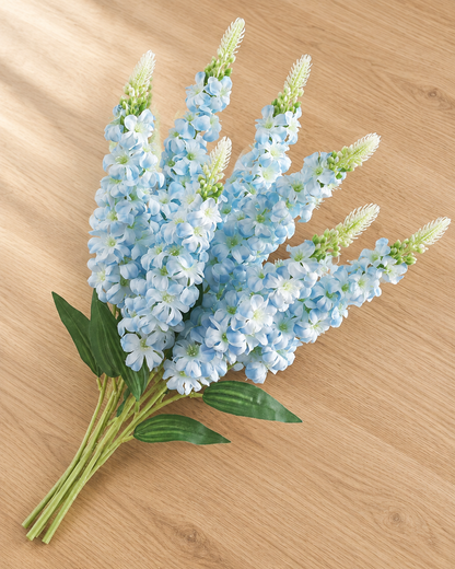 Close-up detail of the light blue artificial delphinium flower stems on an oak table