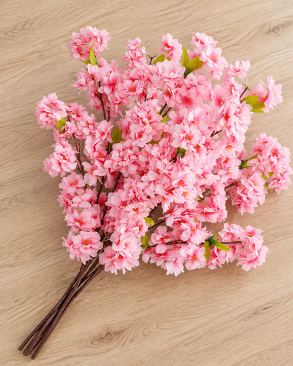 Close-up detail of the pink artificial cherry blossom branch on an oak table