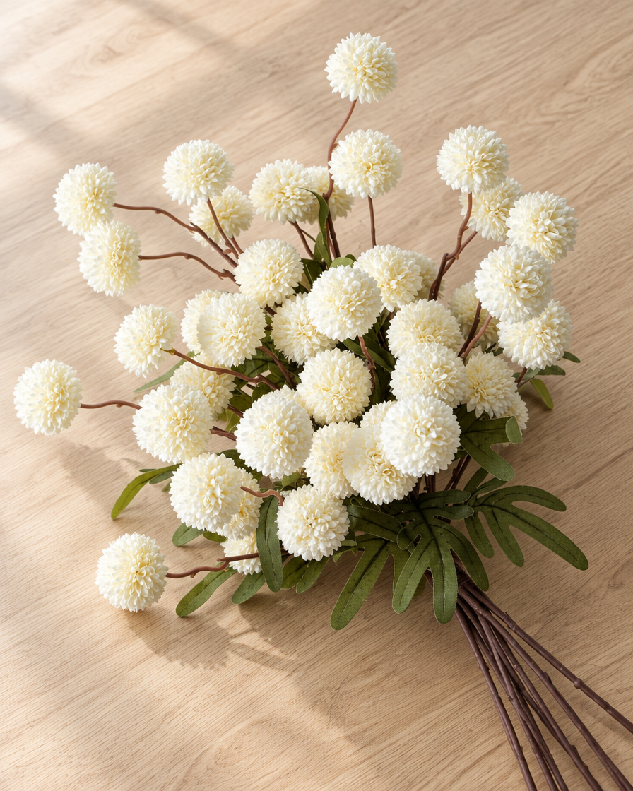 Close-up detail of the white artificial pom-pom flower stems on an oak table