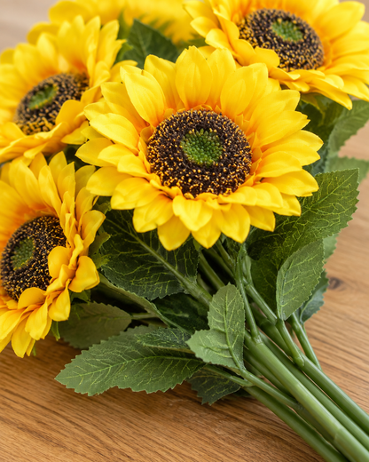 Close-up detail of the yellow artificial sunflower bunch with long stems on an oak table