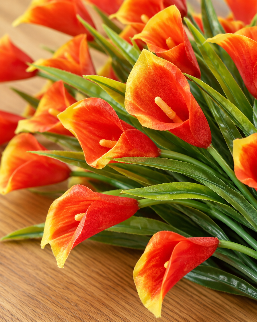Close-up detail of the orange artificial calla lily bunch on an oak table