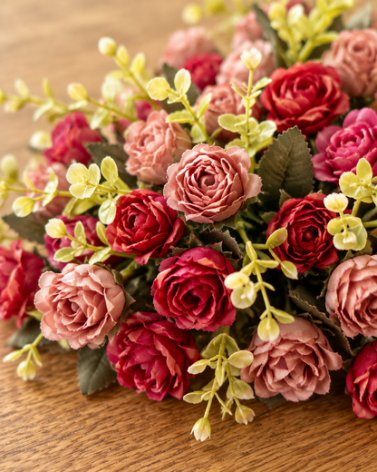 Close-up detail of the red and dusty pink artificial rose bouquet on an oak table