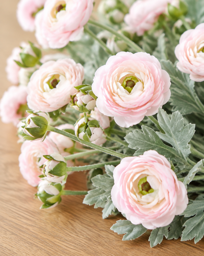 Close-up detail of the pale pink artificial ranunculus stems on an oak table