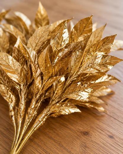 Close-up detail of the gold glitter artificial leaf stems bunch on an oak table
