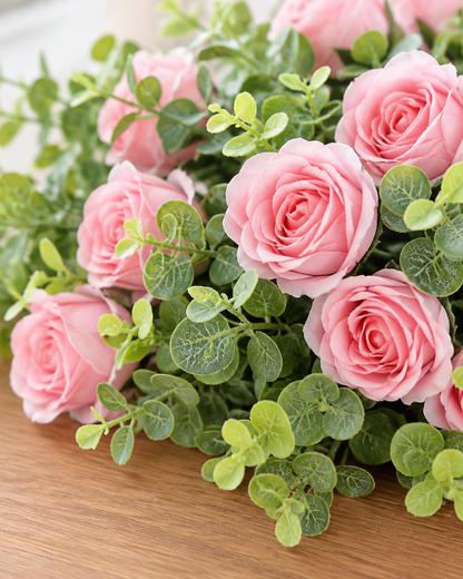 Close-up detail of the pink artificial rose bouquet with greenery on an oak table
