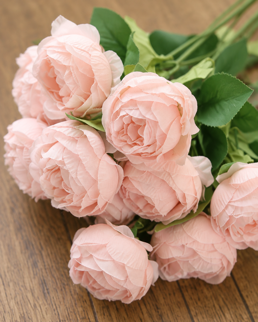 Close-up detail of the soft pink artificial rose bunch on an oak table