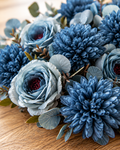 Close-up detail of the dusty blue artificial rose & chrysanthemum bouquet on an oak table