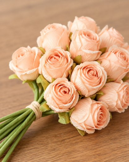 Close-up detail of the peach artificial rosebud bouquet on an oak table