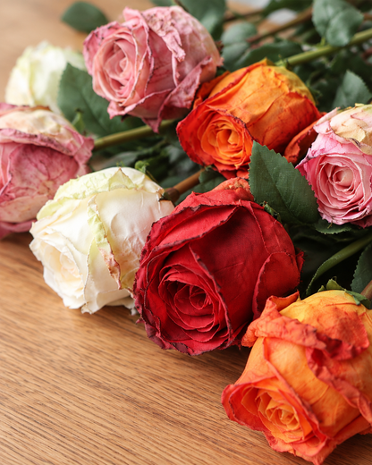 Close-up detail of the multicolour artificial burnt-edge rose stems on an oak table