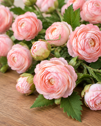 Close-up detail of the pink artificial ranunculus stems on an oak table