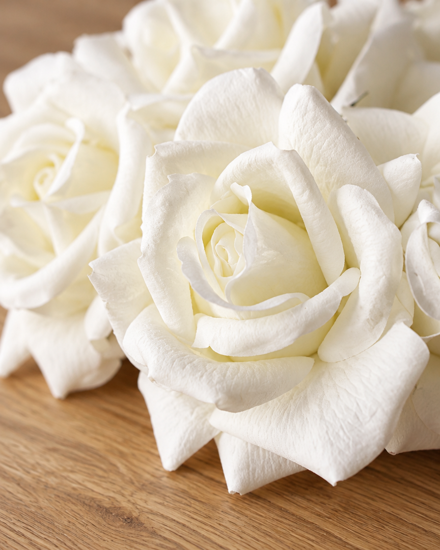 Close-up detail of the white artificial curl-edge rose bouquet on an oak table