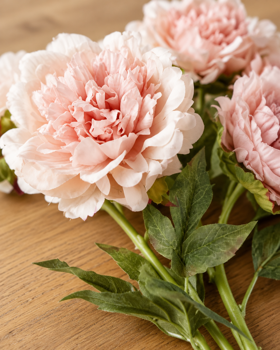 Close-up detail of the blush pink artificial peony stems on an oak table