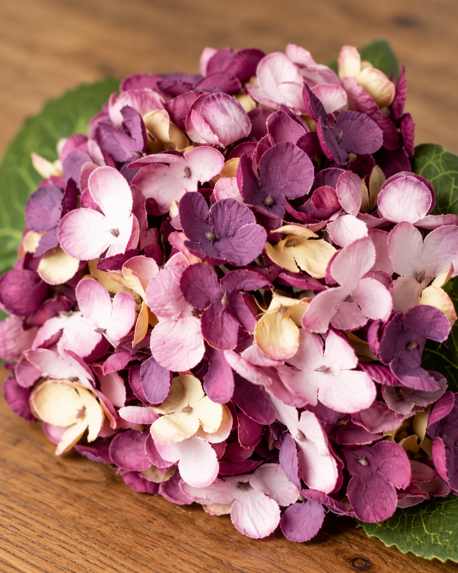 Close-up detail of the plum purple artificial hydrangea stem on an oak table