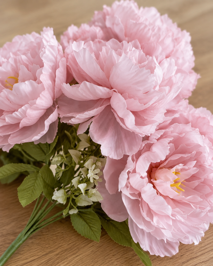 Close-up detail of the soft pink ruffled artificial peony bouquet on an oak table