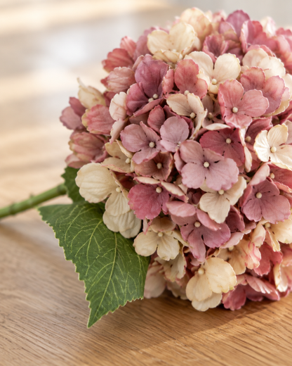 Close-up detail of the dusty pink artificial hydrangea stem on an oak table