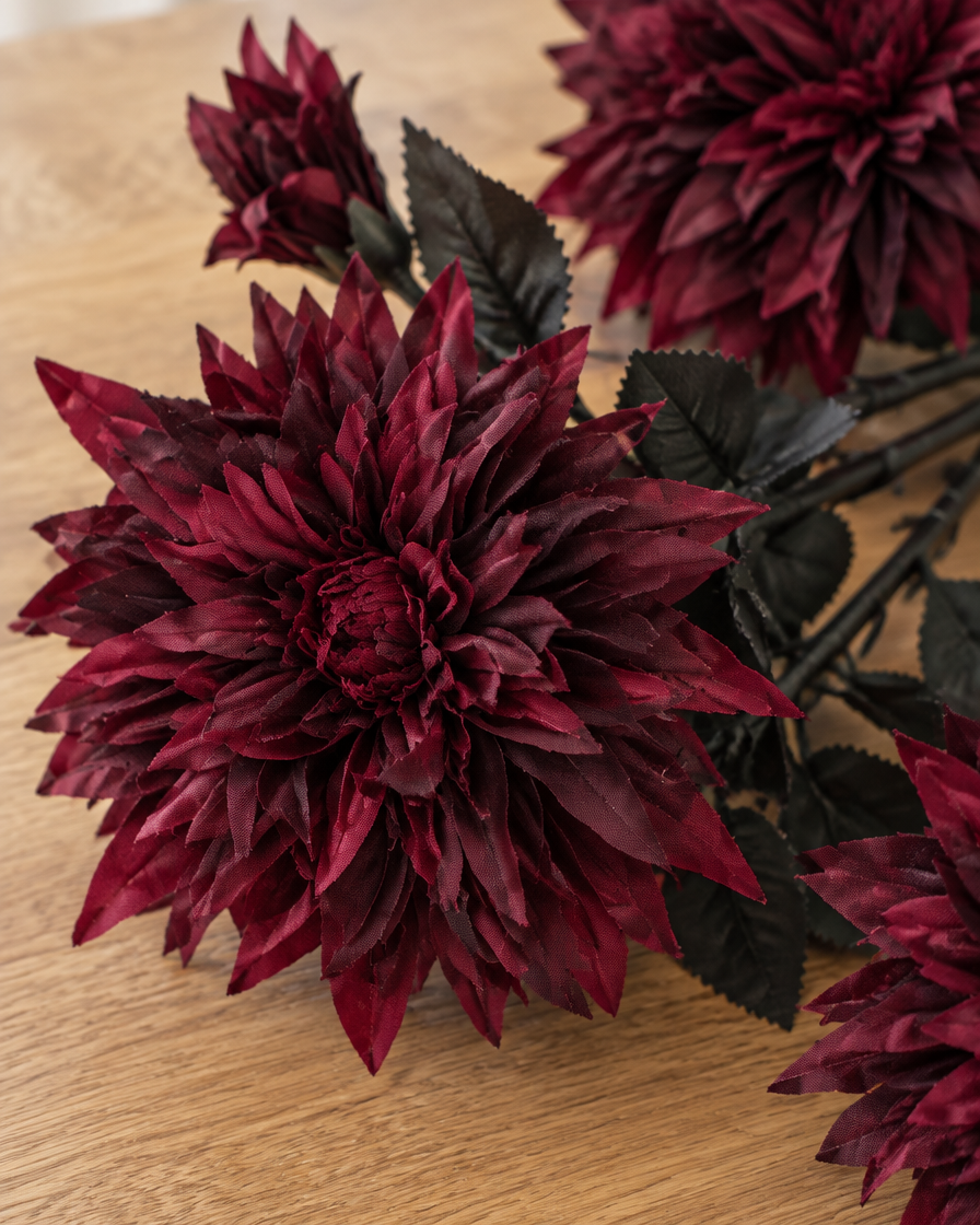 Close-up detail of the burgundy artificial dahlia stems on an oak table