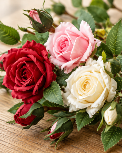 Close-up detail of the red pink and cream artificial rose branches on an oak table