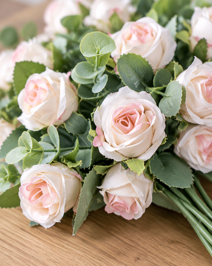 Close-up detail of the blush pink artificial rose & eucalyptus bouquet on an oak table