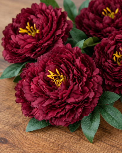 Close-up detail of the burgundy artificial peony bunch on an oak table