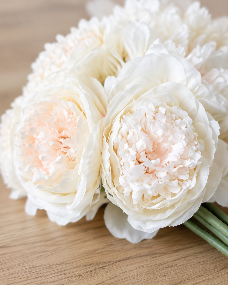 Close-up detail of the ivory white artificial peony bunch on an oak table