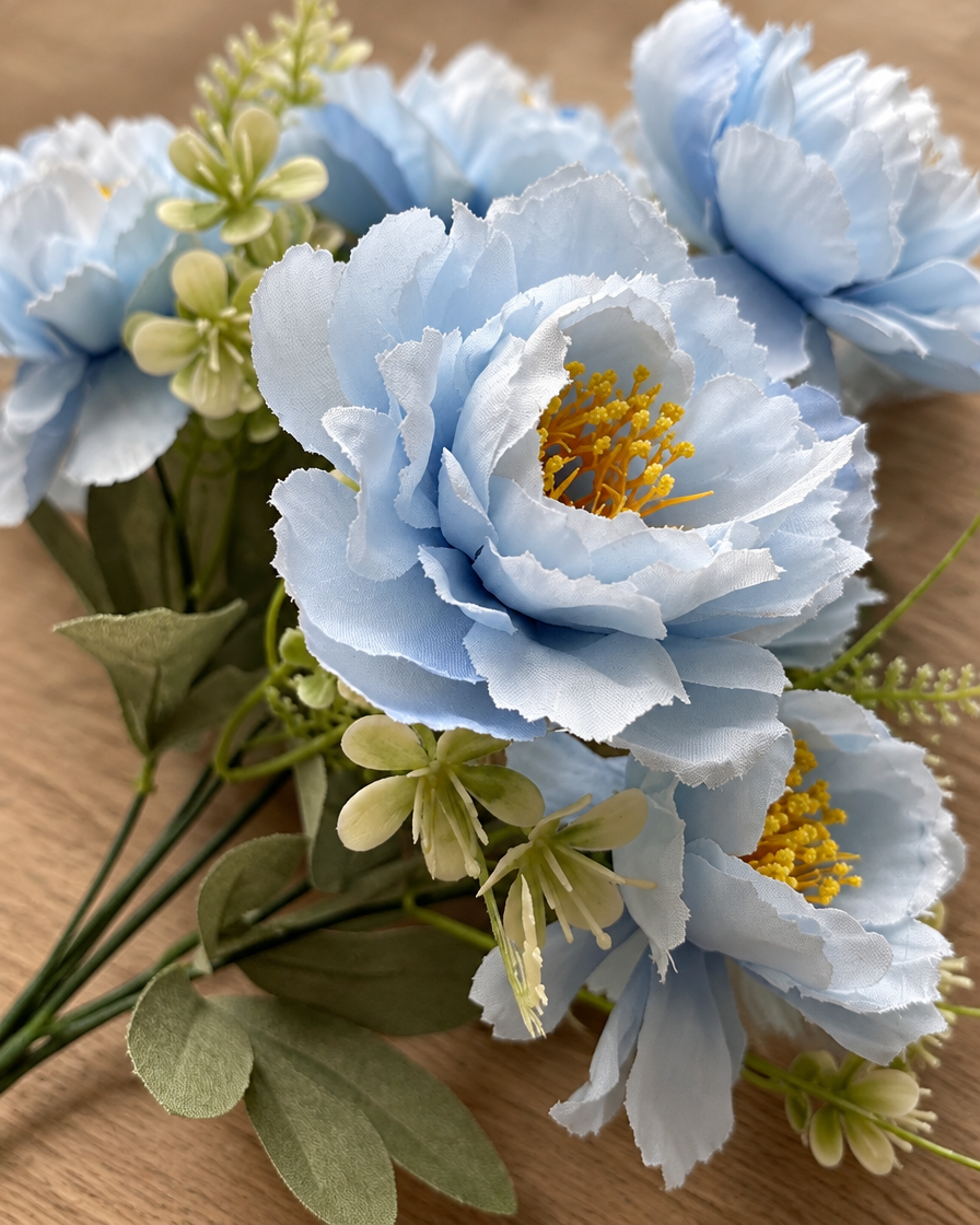 Close-up detail of the light blue artificial peony bunch on an oak table