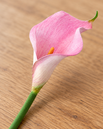 Close-up detail of the pink artificial calla lily stem on an oak table