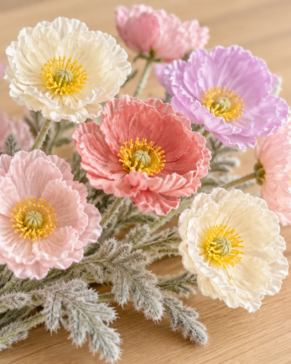 Close-up detail of the pastel mixed artificial poppy stems on an oak table